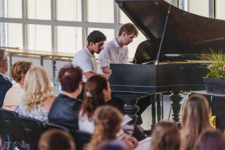 Zwei Schüler spielen gemeinsam Piano vor Publikum in einem festlichen Raum.