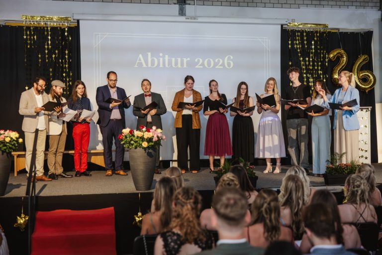 Schülergruppe bei der Abiturfeier 2026 auf der Bühne mit Urkunden.