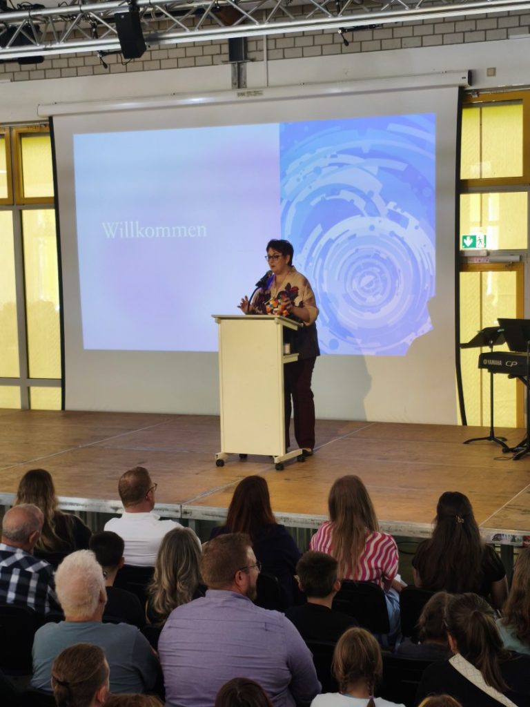 Eine Person steht an einem Redepult vor einer Präsentation mit dem Titel "Willkommen".