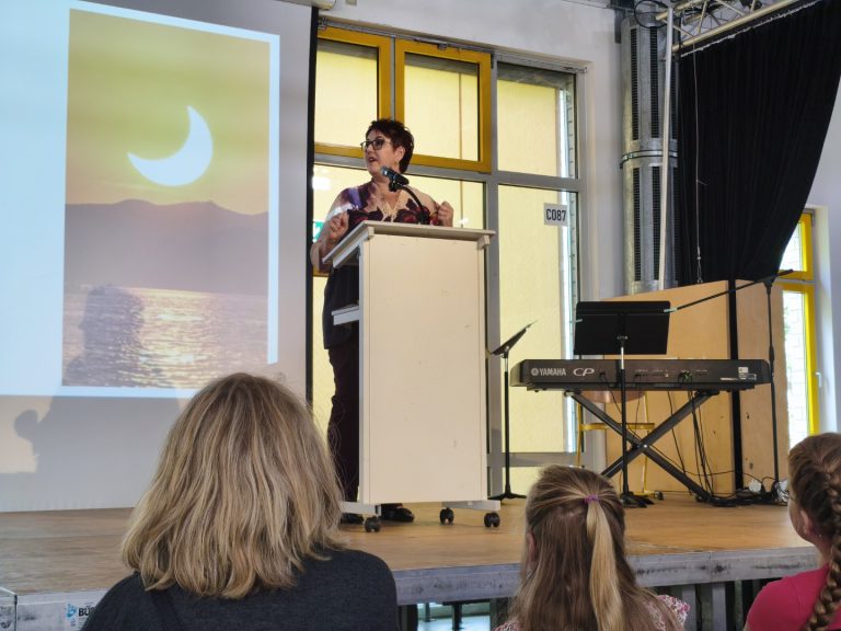 Frau am Rednerpult mit Bild einer Halbmondsicht im Hintergrund. Bühnenumgebung.