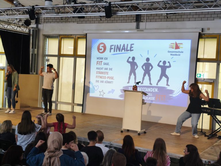 Schüler präsentieren eine Fitness-Pose auf der Bühne während einer Schulveranstaltung.