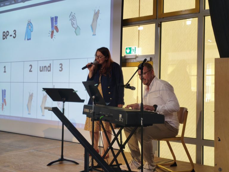Sängerin am Mikrofon, Pianist spielt, im Hintergrund eine Präsentation.