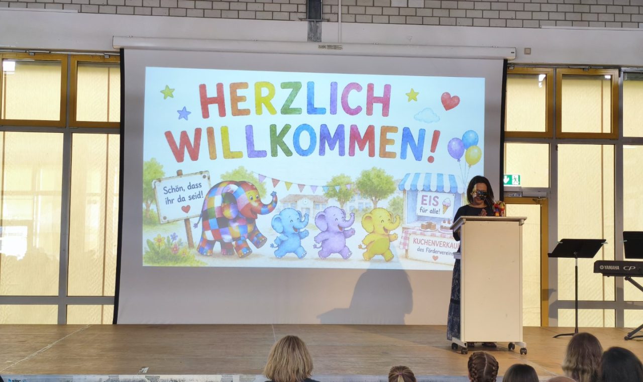 Eine Präsentation mit dem Text "Herzlich Willkommen" auf einer Bühne.