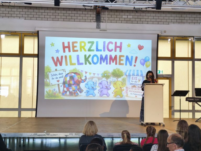 Eine Präsentation mit dem Text "Herzlich Willkommen" auf einer Bühne.