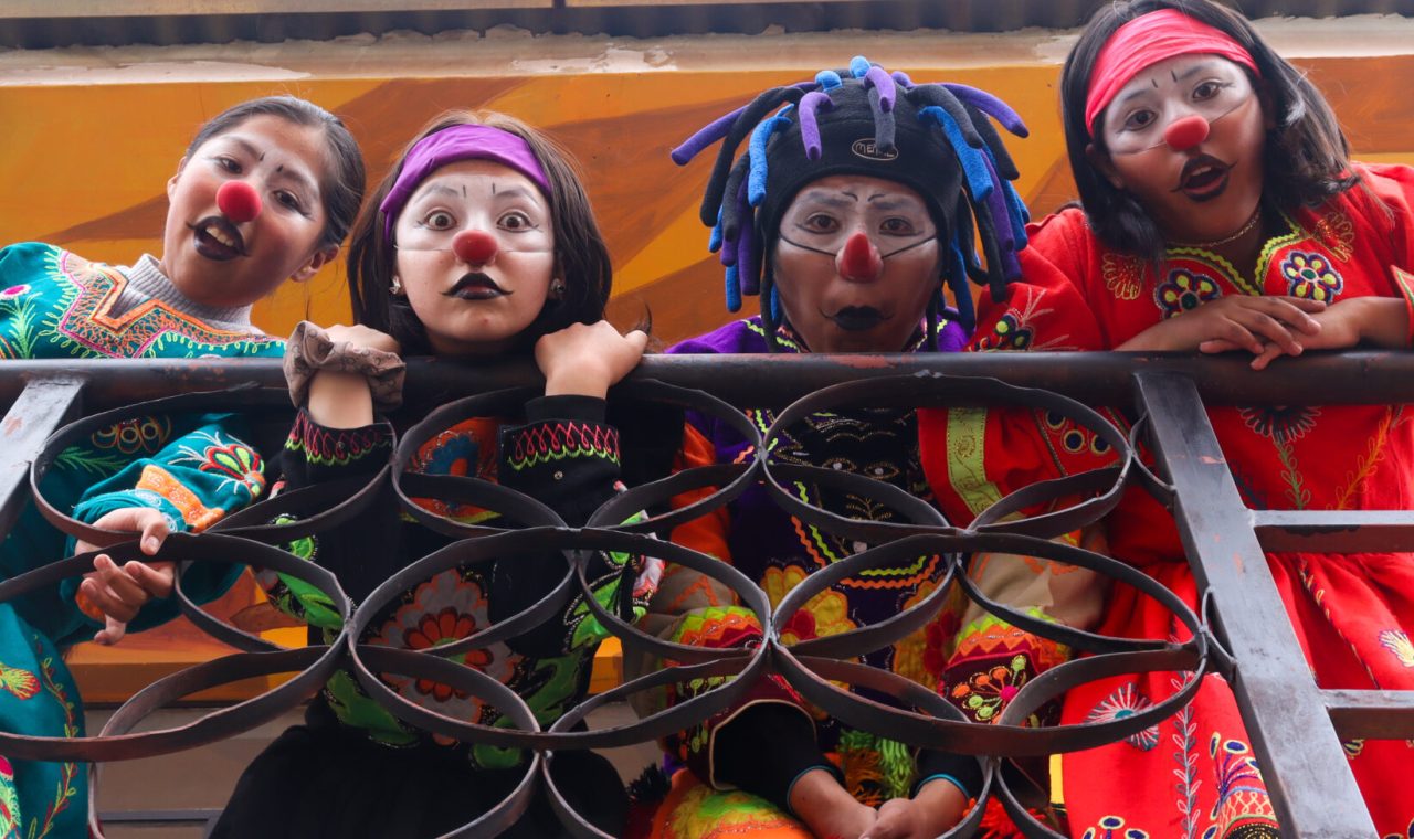 Vierte Kinder in bunten Kostümen und Clownschminke hängen von einem Geländer.