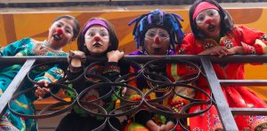 Vierte Kinder in bunten Kostümen und Clownschminke hängen von einem Geländer.