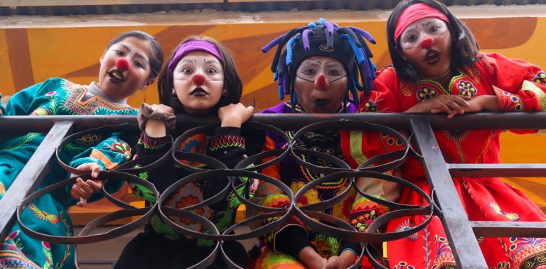 Vier Kinder in bunten Clownskostümen schauen über ein Geländer.