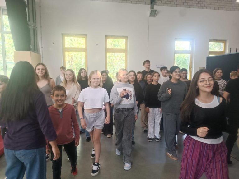 Schülerinnen und Schüler stehen in einem Raum und bewegen sich zur Musik.