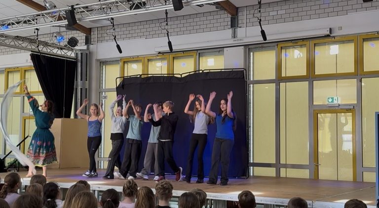Schüler führen eine Tanzaufführung auf einer Bühne vor Publikum auf.