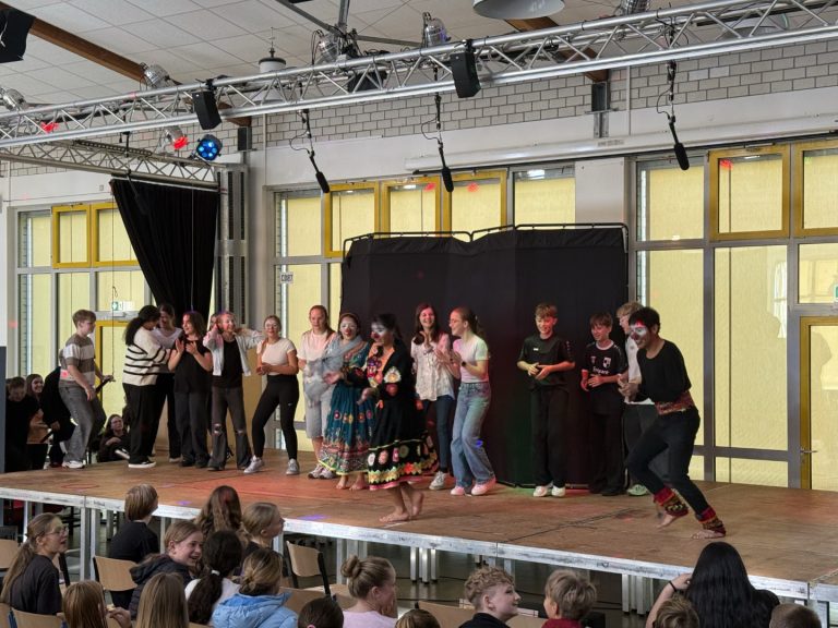 Schüler präsentieren eine Aufführung auf einer Bühne in der Schulhalle.